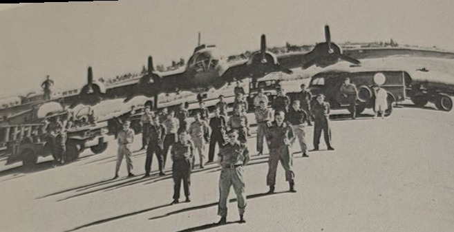 A row of B-17 Flying Fortress bombers with aircrew standing in front on an airfield apron